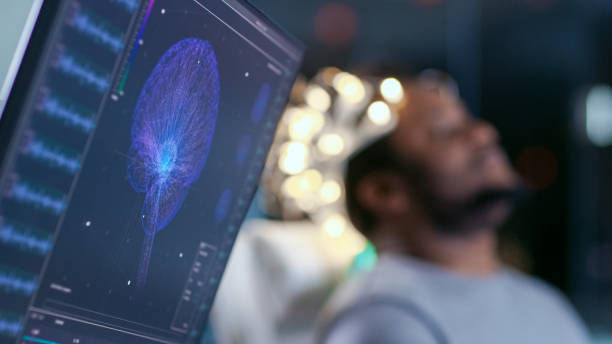 Computer screen showing a blue brain scan, with a person sitting in the background. The setting is a modern lab, lights softly glowing.