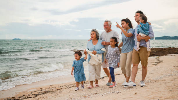 Family walking on a beach, smiling and pointing at the sea. Sand, ocean waves, and a cloudy sky create a joyful, relaxed setting.