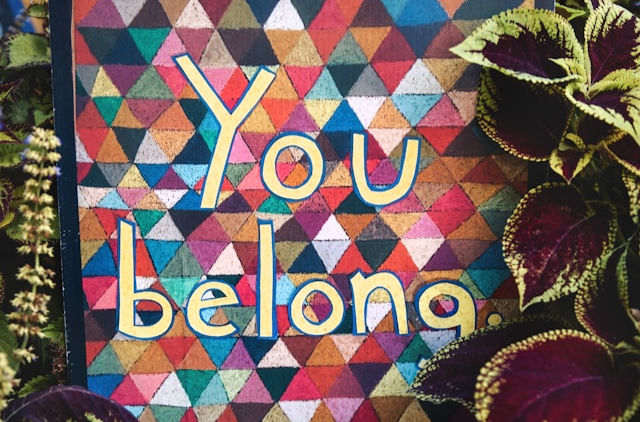 Colorful geometric pattern with "You belong" text. Surrounded by purple and green plants, creating a welcoming and inclusive vibe.