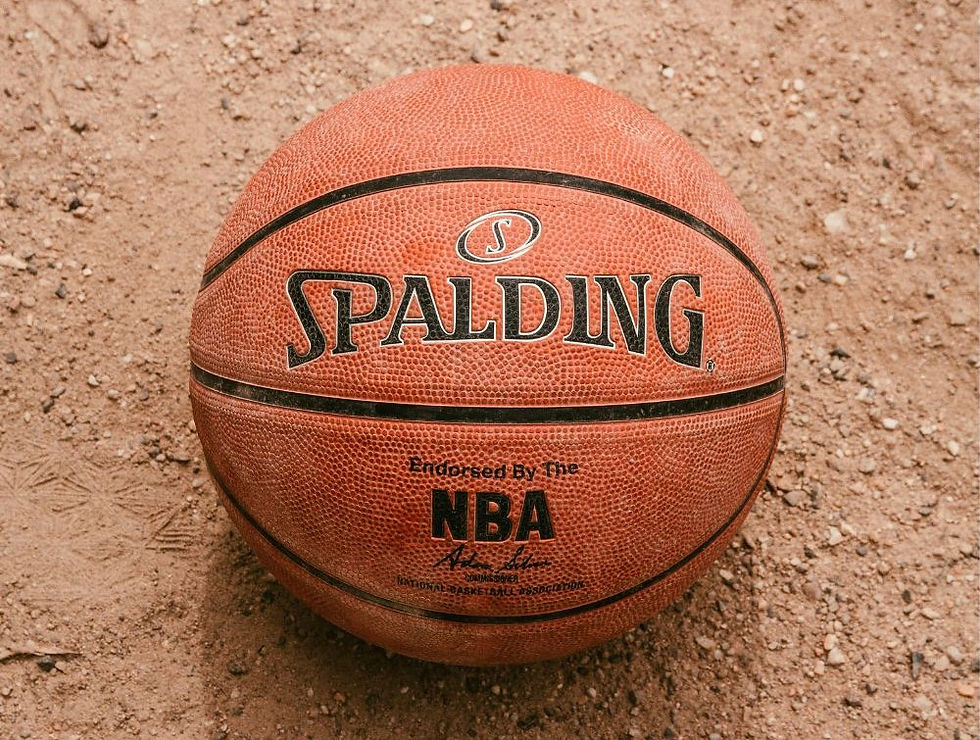 A Spalding basketball rests on a sandy surface. Visible text includes "Spalding" and "Endorsed by the NBA." Earthy tones dominate the image.