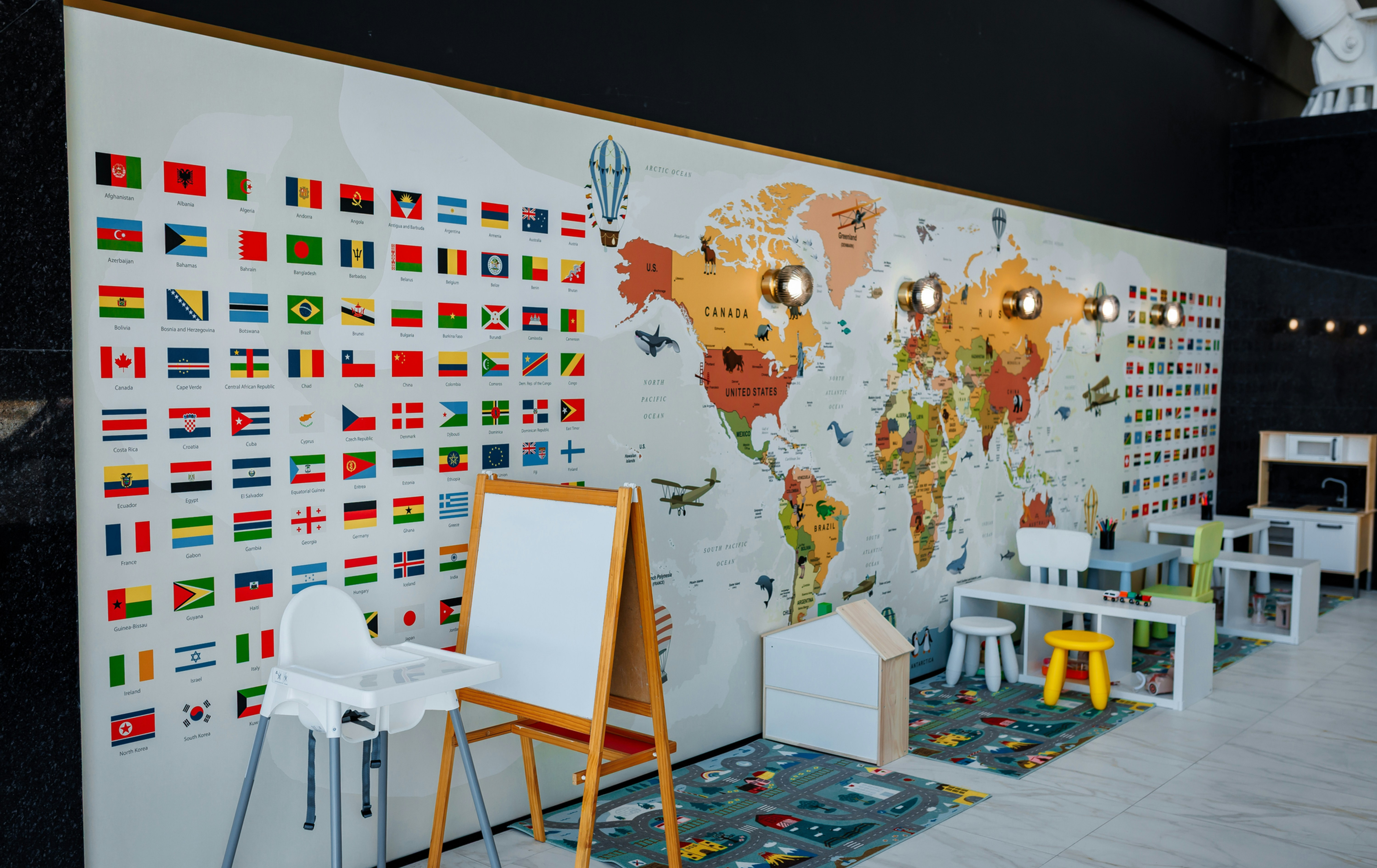 Kids playroom with world map and country flags, easel, high chairs, colorful rugs, and #swag party and snapmaster text.