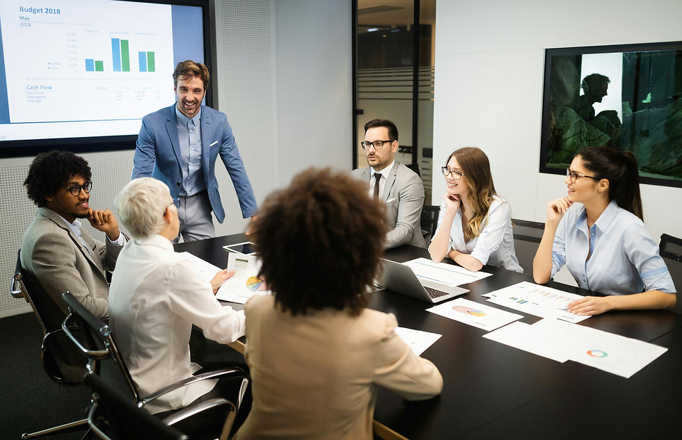 Business team meeting as a man presents Budget 2018 charts on a screen; coworkers review papers and smile.