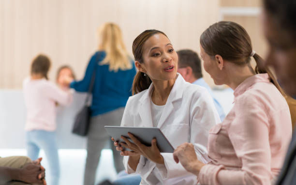 Smiling nurse in blue scrubs with a stethoscope talks to a patient in a bright clinic.