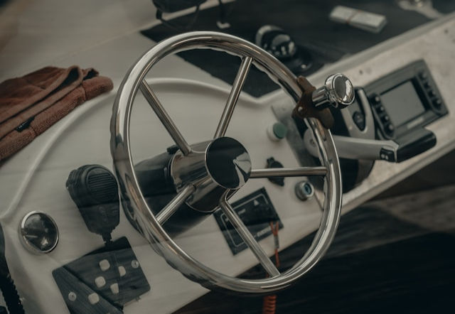 Boat steering wheel with controls and radio on a dashboard. Silver, metallic tones dominate, creating a nautical and mechanical vibe.