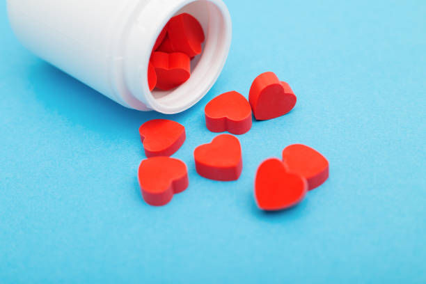 Red heart shaped pills with plastic bottle on blue background.