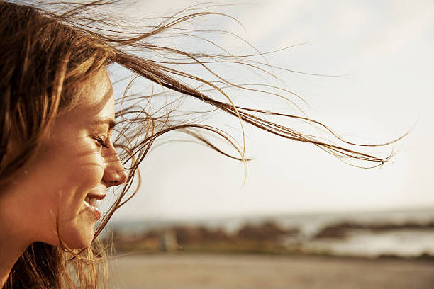 Woman with arms outstretched on a hill, facing a blurred cityscape; white top, floral skirt, windy and free-spirited.