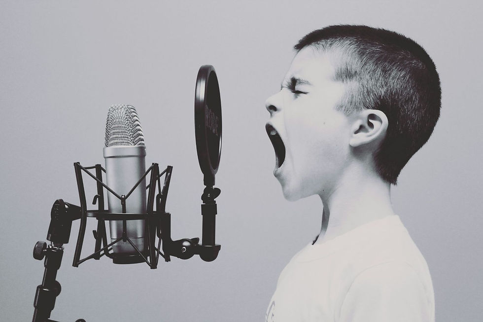 A black-and-white image of a boy shouting into a microphone. The background is plain, and the mood is expressive and intense.
