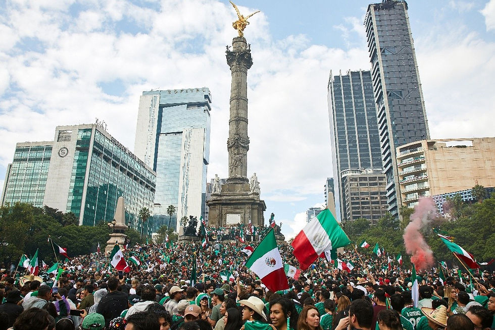 Crowd waving Mexican flags at the Angel of Independence in Mexico City, with skyscrapers behind and a festive, protest-like mood.