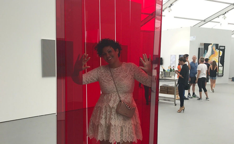 Smiling woman in a red translucent art installation at a gallery, with visitors and drinks in the background.