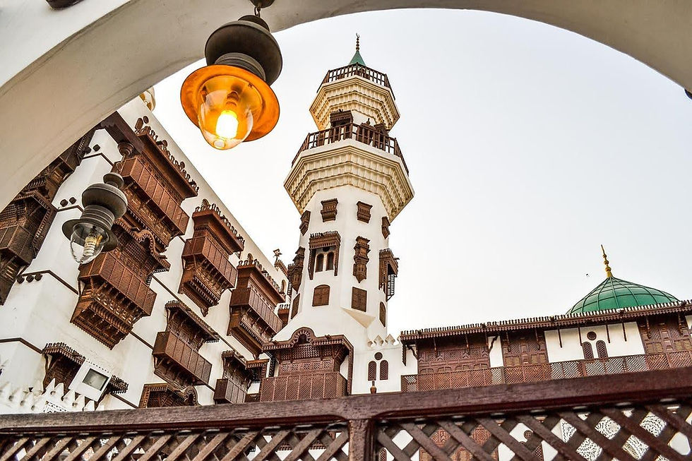 Ornate white and brown building with wooden lattice windows and a tall tower under a clear sky. An archway with glowing lights frames the view.