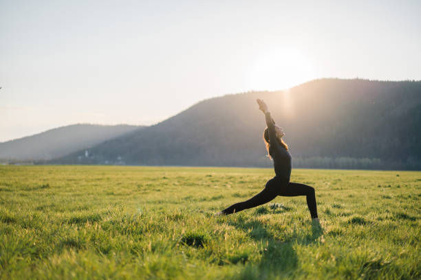 Woman in black yoga pose in a green field at sunrise, with mountains silhouetted in the background.