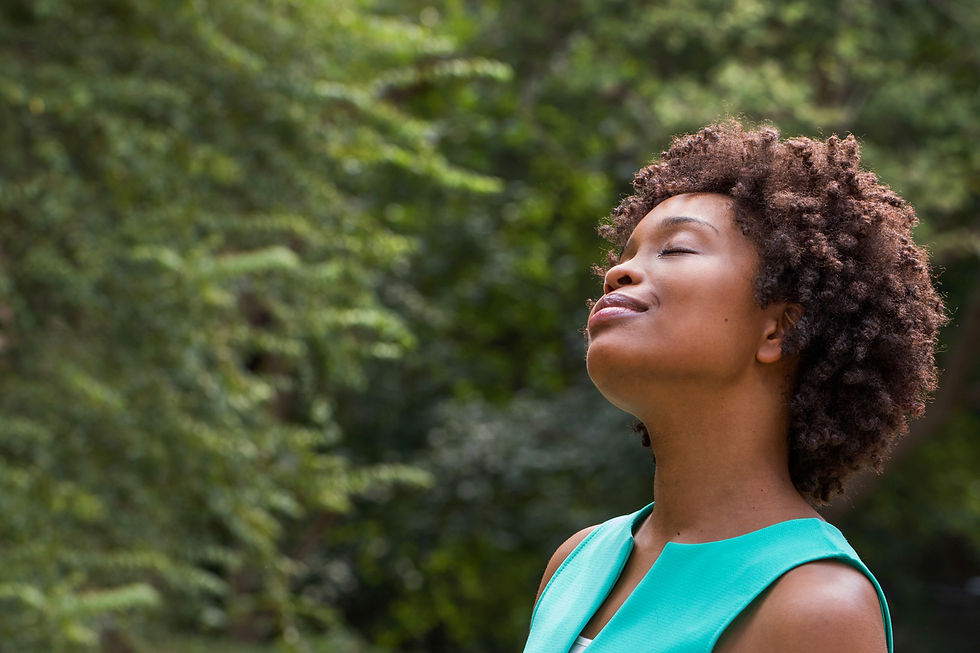 Woman in a turquoise top with closed eyes, enjoying nature. Greenery fills the background, creating a serene, peaceful mood.