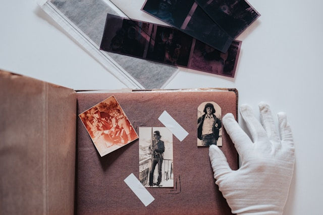 Gloved hand flipping a scrapbook page with vintage photos and negatives. Warm tones create a nostalgic mood.