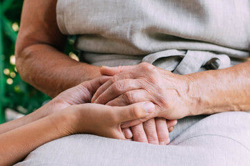 Child gently with love holds hand of old grandmother