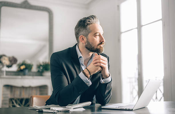 Businessman working from home sitting with a pile of loose paperwork and a laptop computer