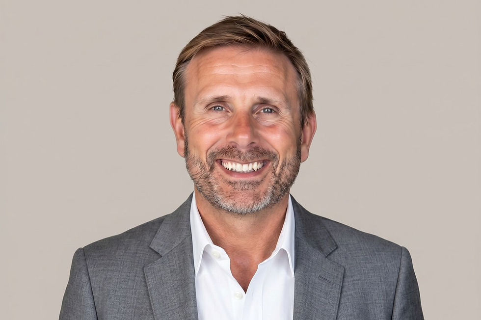 Smiling man in a gray suit and white shirt against a plain beige background, looking confident and friendly