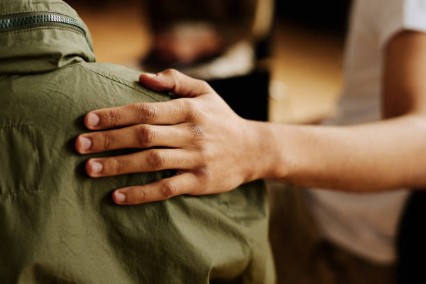 A hand rests supportively on a person's shoulder in a green shirt. The background is softly blurred, evoking a warm, caring mood.
