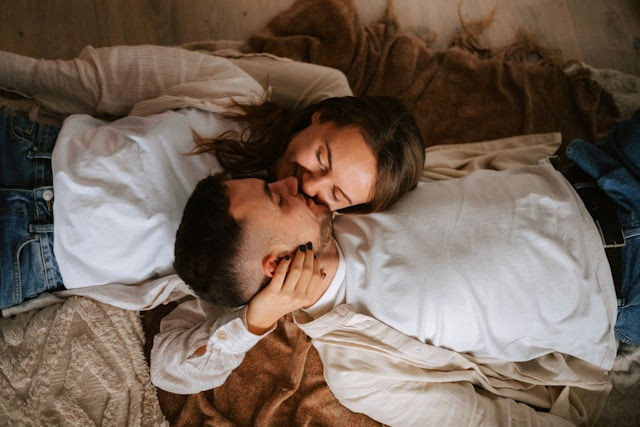 The photo shows a couple lying together on a soft blanket, sharing a tender moment with their faces close, smiling and enjoying each other's company.