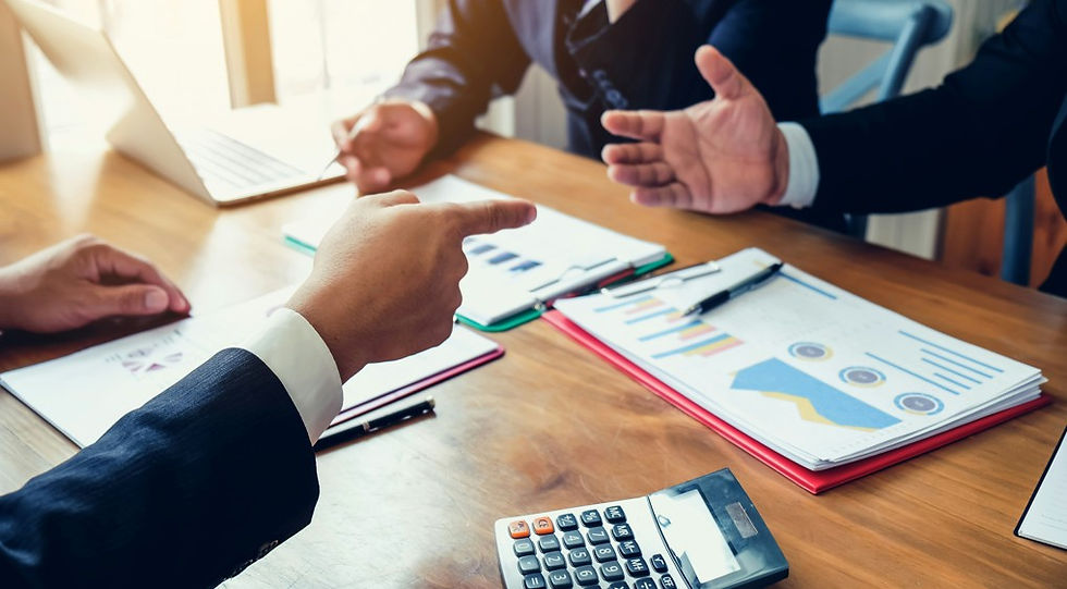 Business meeting with hands gesturing over chart-filled reports, laptop and calculator on a wooden table in a bright office.