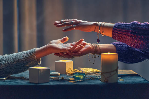 The image depicts a mystical palm reading session, where a fortune teller in a purple sweater, adorned with rings and bracelets, hovers her hands over a client’s open palm.