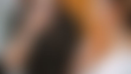 Two people in therapeutic gestures; one in focus, touching neck, wearing white. Background person in brown, soft light, calm setting.