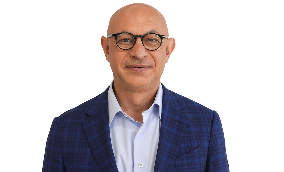 Bald man with glasses wearing a blue plaid suit and light blue shirt, smiling slightly against a plain white background.