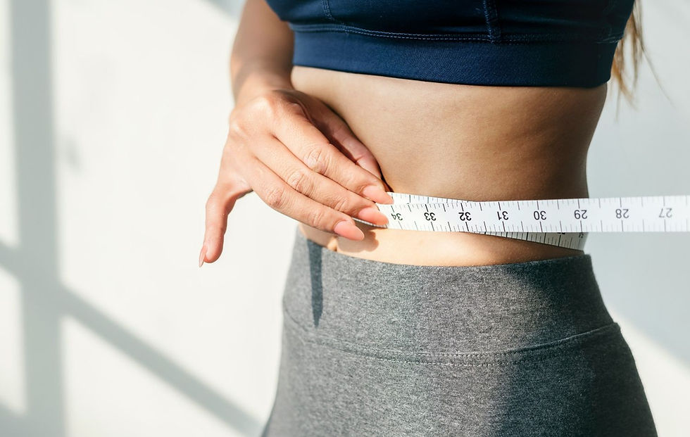 A person measures their waist with a tape in bright light. They're wearing a navy top and gray leggings. The tape shows numbers clearly.