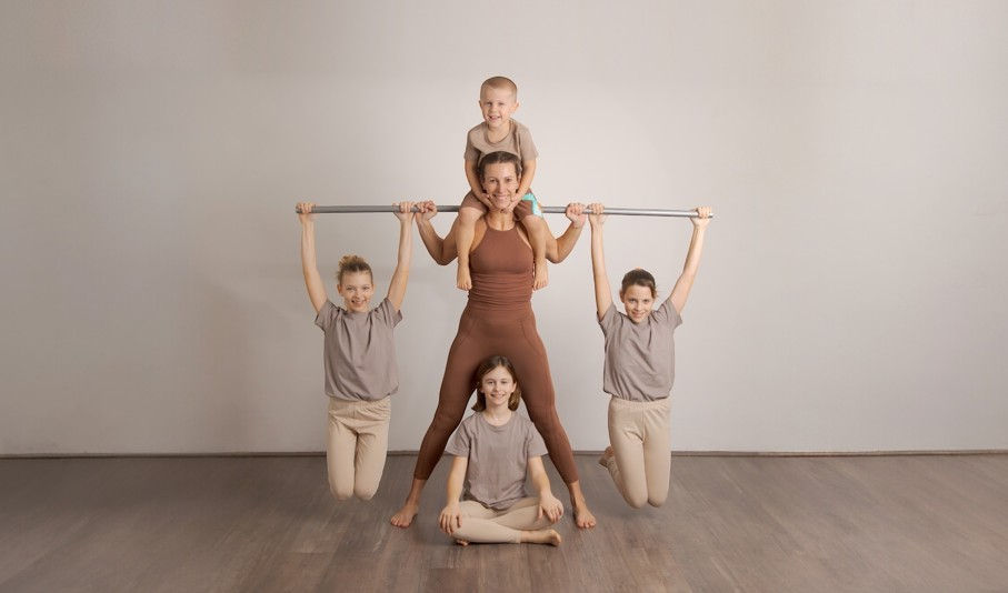 Woman and four children pose in a studio, two hanging from a bar, one on her shoulders, one seated cross-legged, smiling