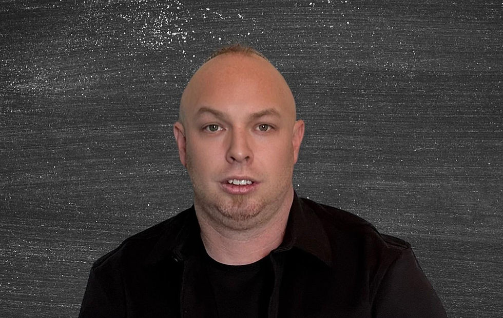 A person in a black shirt is in front of a textured dark background, appearing neutral and focused. No visible text.