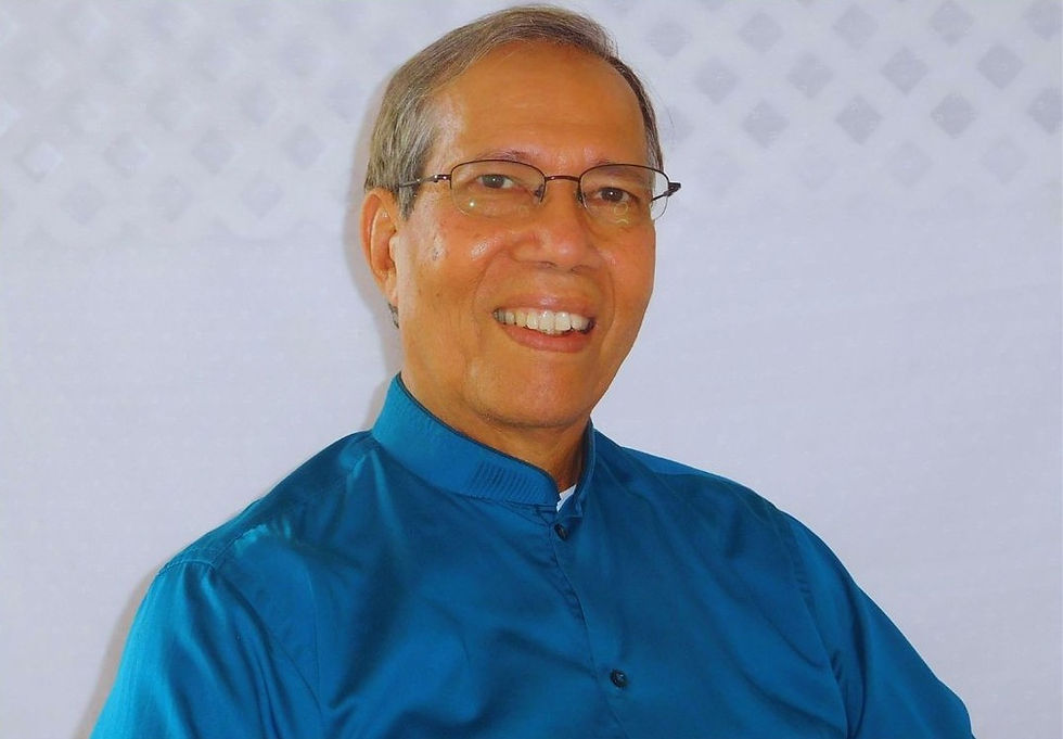 Smiling man in glasses wearing a blue shirt, against a white patterned background. Bright, cheerful mood.
