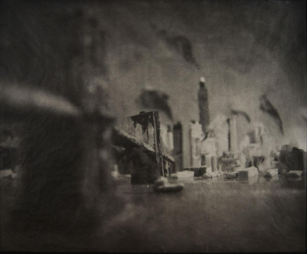 Blurry black-and-white city skyline and bridge model on a tabletop, with tall buildings fading into a hazy background.