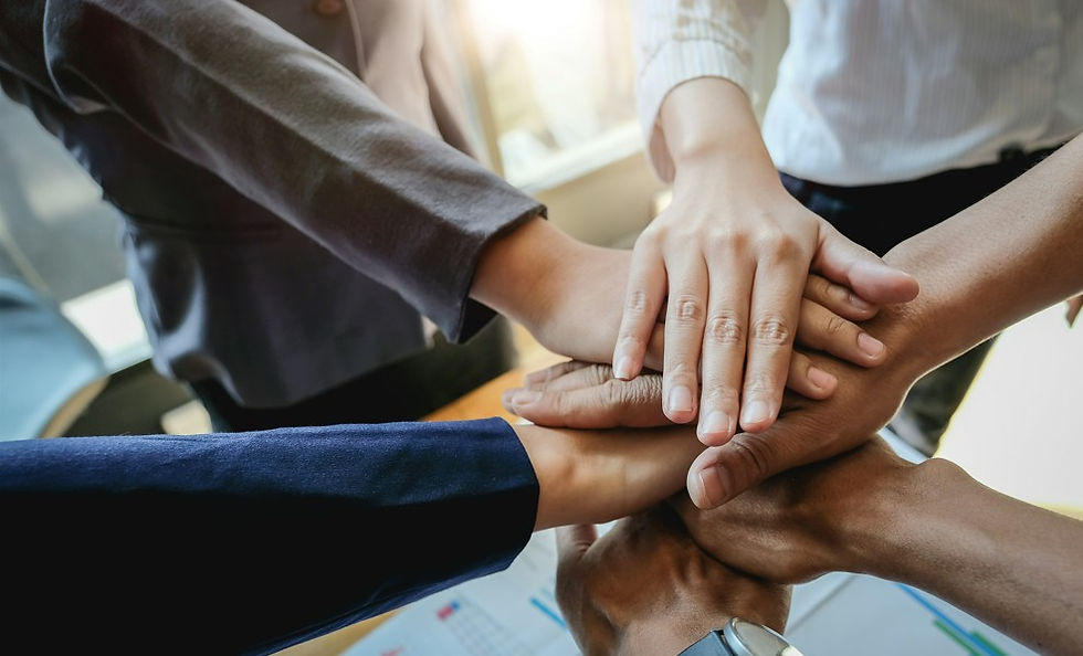 Team members stack hands in a collaborative huddle over a bright office table, showing unity and support.