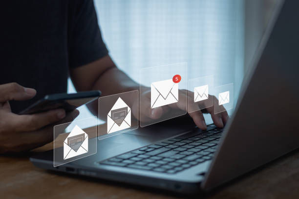 Person using a phone and laptop with floating email icons, one with a red 5 notification badge, in a dim office setting
