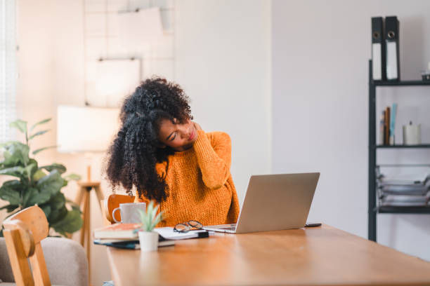 woman massaging her neck, indicating discomfort or strain while working on a laptop at home