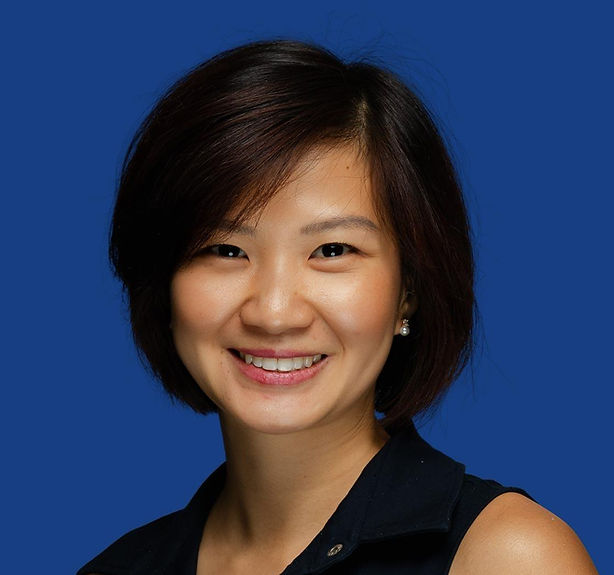 Smiling woman with short dark hair against a blue background. Wearing a black top. The mood is cheerful and welcoming.