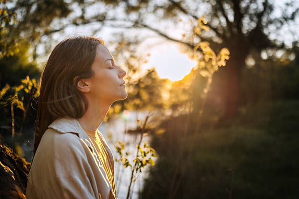 Young woman in profile with eyes closed at sunset by the water, bathed in warm golden light, calm and reflective.