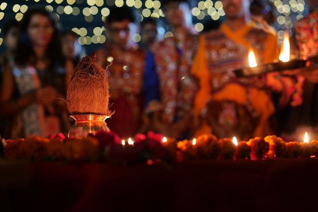 People in colorful dress hold lit lamps during a glowing candlelight ritual, with marigolds and bokeh lights in the background