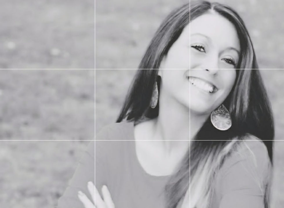 Black-and-white portrait of a smiling woman with long dark hair and earrings, outdoors against a blurred background.