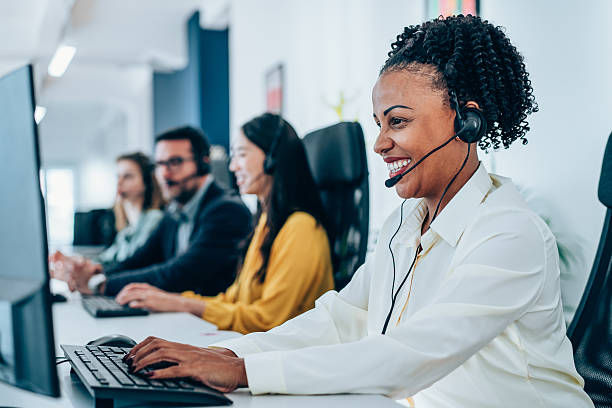 Four diverse call center agents in headsets work and smile at computers in a bright office, creating a positive and professional mood.