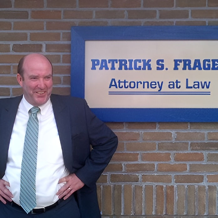 Man in a suit standing confidently by a brick wall next to a sign reading "Patrick S. Frager, Attorney at Law."