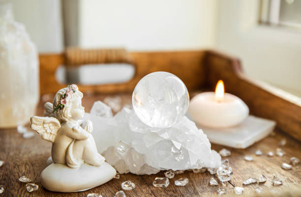 A serene scene with a cherub figurine, crystal ball, and lit candle on a wooden tray. Scattered clear crystals create a peaceful ambiance.