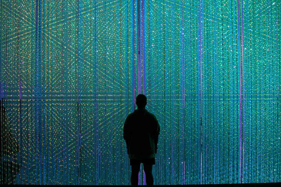 Silhouette of a person facing a vibrant, illuminated curtain of green and blue lights, creating a serene, futuristic atmosphere.