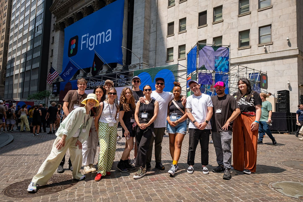 Smiling group posing outside a building with giant Figma banners and flags on a sunny city street.