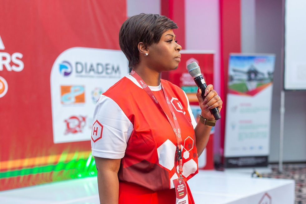 Woman in red and white attire speaks into a microphone on stage, with red and white banners and posters in the background.