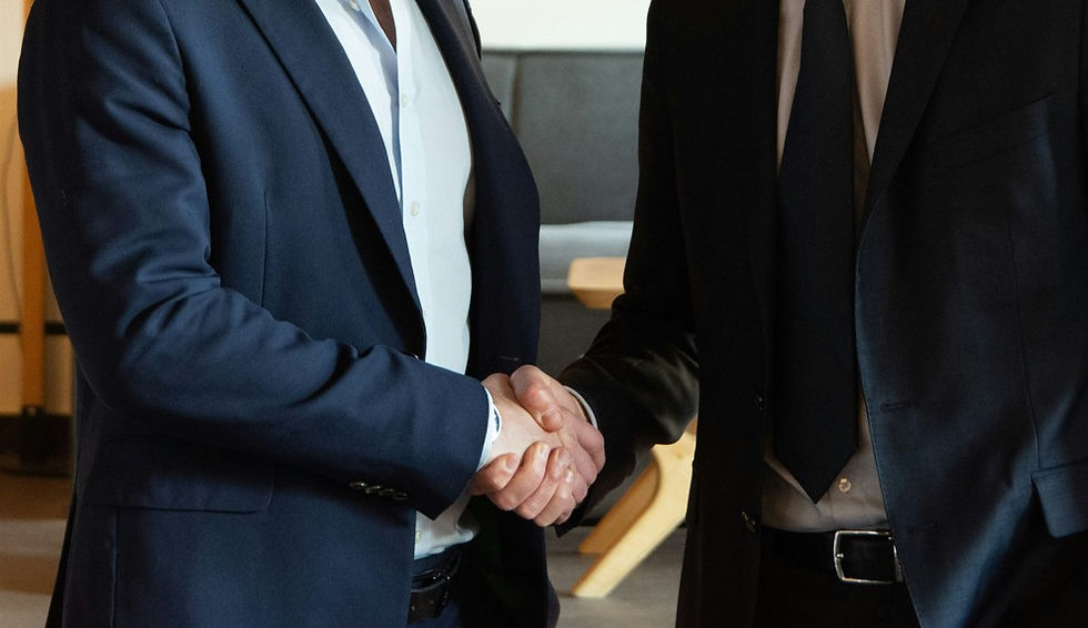 Two businessmen in dark suits shake hands in a modern office, suggesting a formal agreement.