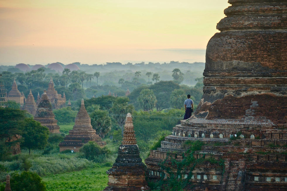 Man stands on an ancient brick temple overlooking misty pagodas and lush greenery at sunrise.