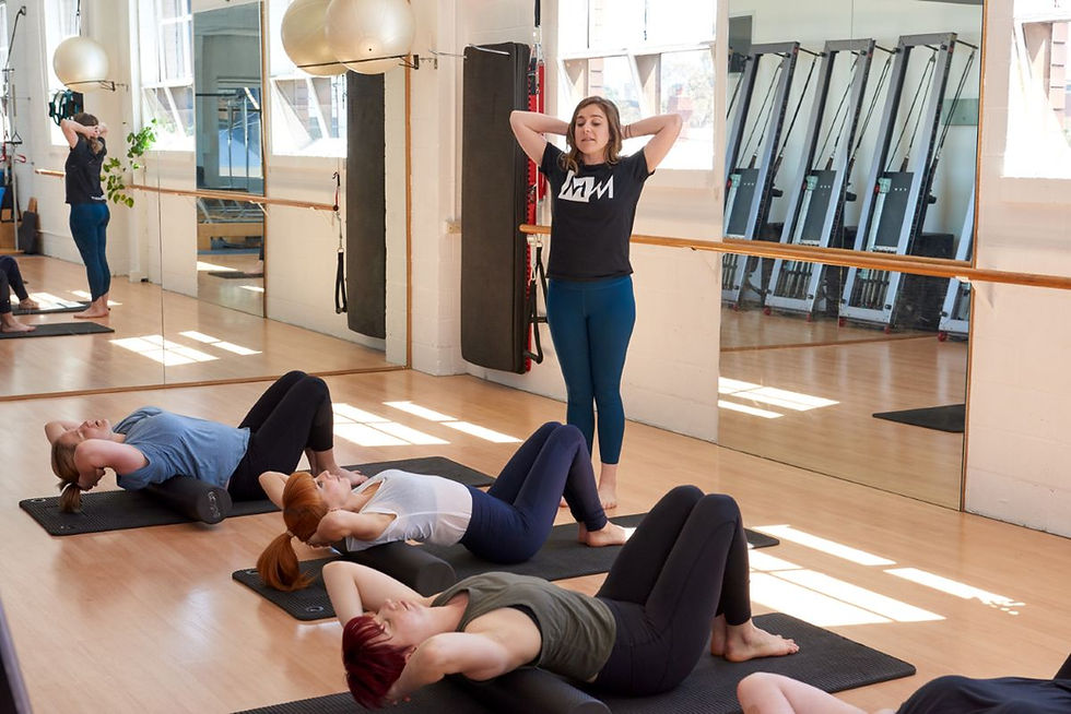 The photo shows a fitness instructor leading a group class in a bright, spacious studio with mirrors and exercise equipment.