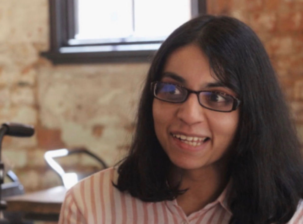 A woman with black hair, wearing eyeglasses having a conversation with someone.
