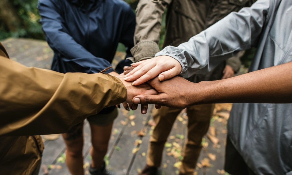 Group of hikers stacking hands in a teamwork huddle on a wooden trail deck outdoors