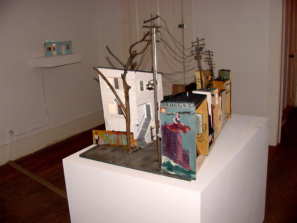 Model of a colorful urban scene on a white pedestal, featuring buildings, signage, and utility poles. A small "Motel" sign is visible.